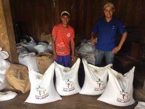 Foto mostra dois agricultores atŕas de sacas de cacau