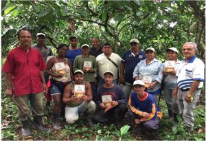 Foto mostra grupo de agricultores e agricultoras com pés de cacau e floresta ao fundo